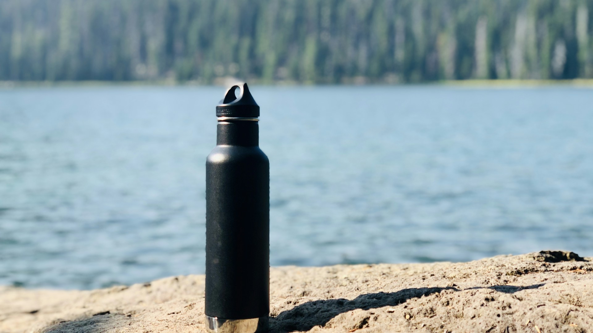 black and gray sports bottle on brown sand near body of water during daytime