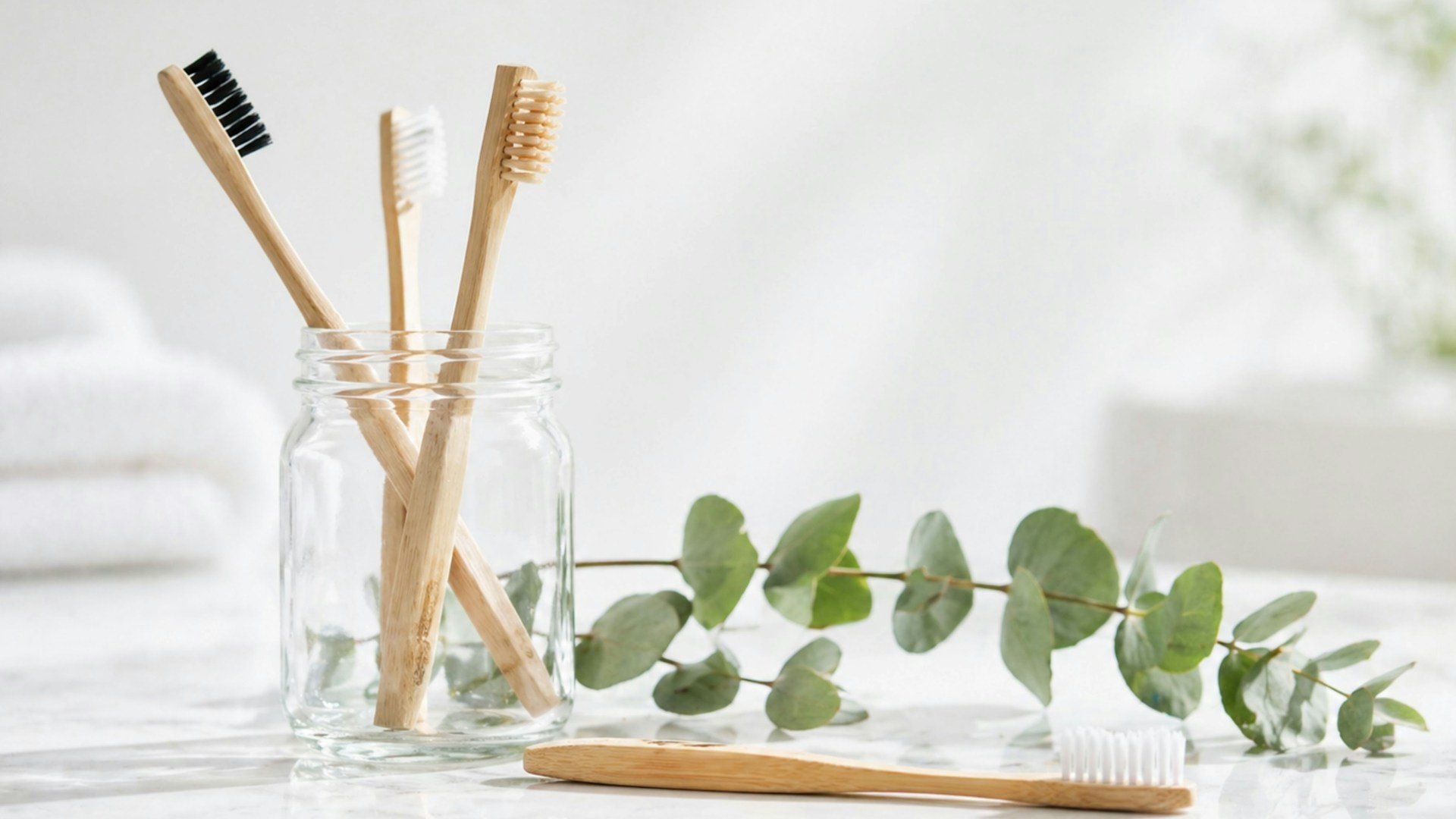 Bamboo toothbrushes in a glass jar with eucalyptus leaves.
